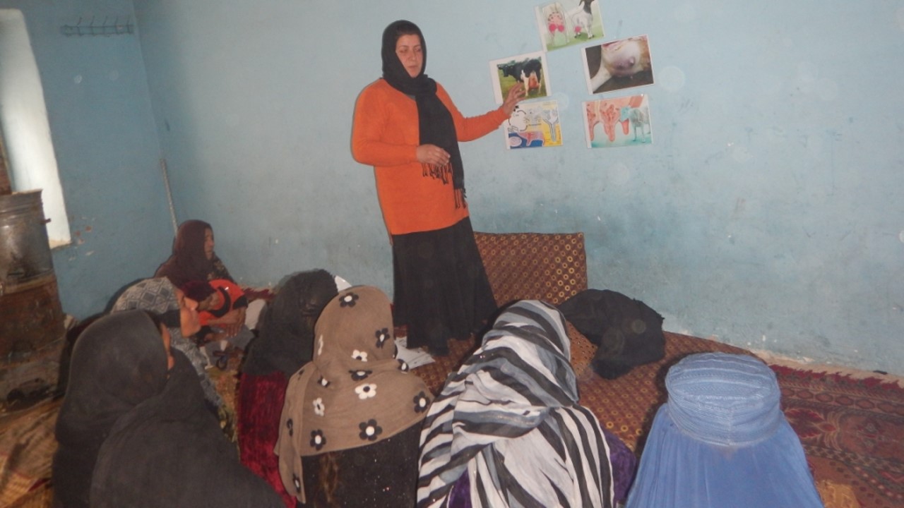 A woman lecturing a group in headscarfs sitting on a floor